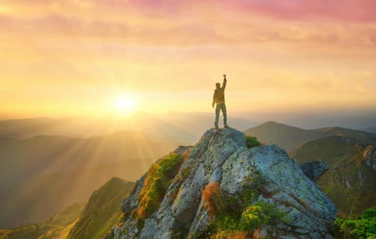 man on mountain top hand raised reaching goal