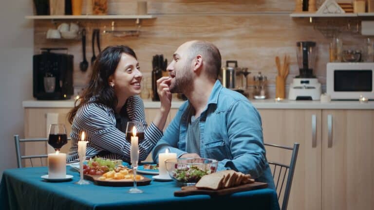 Couple laughing at dinner table at home as laughing is good for the relationship and good for the soul