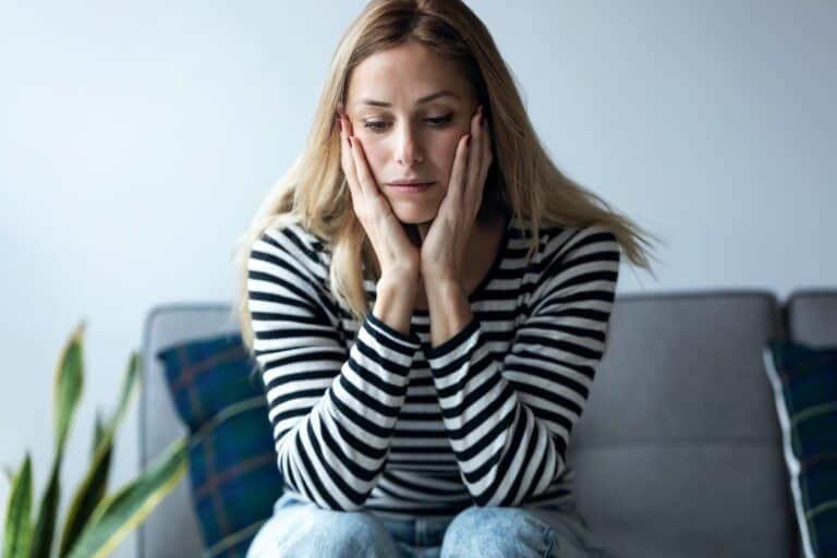 Depressed young woman sitting on couch thinking about what to do