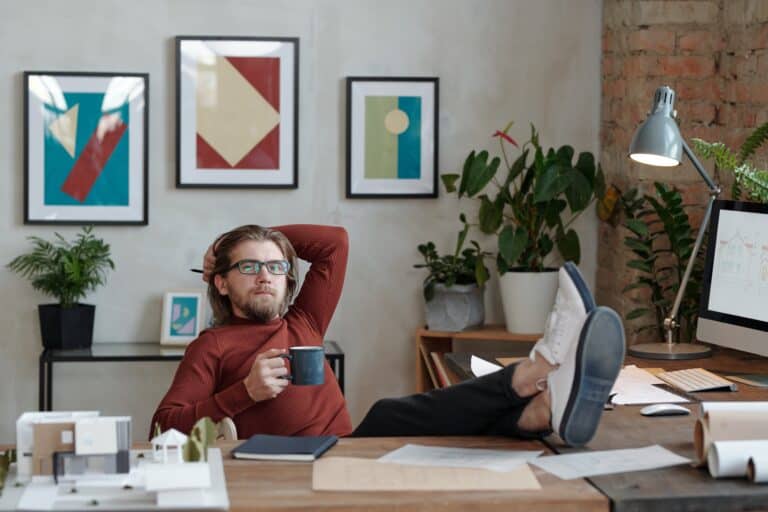 Young relaxed architect with cup of coffee looking at you while thinking of ideas for new project