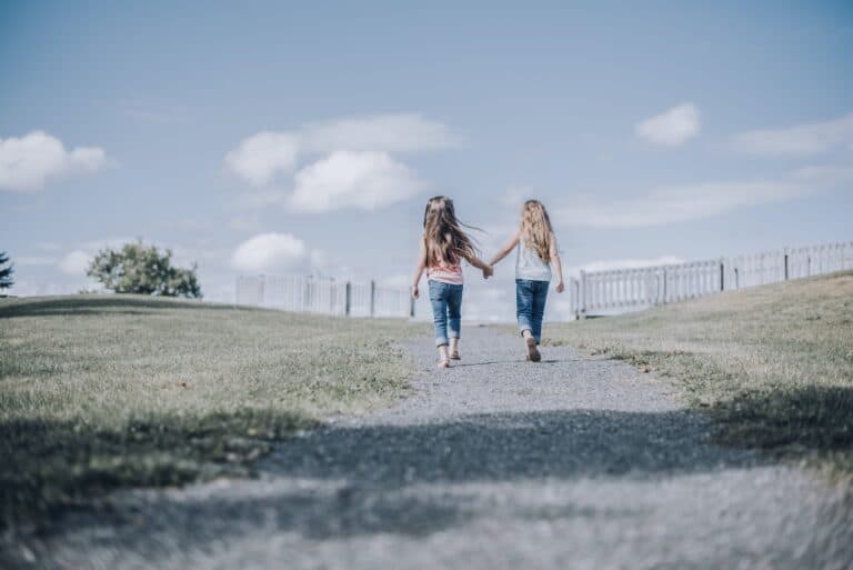 two young children, girls, walking hand in hand down a road