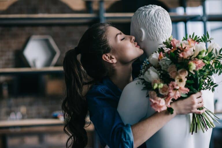 young woman with bouquet of flowers hugging a male manikin dreaming of a real relationship