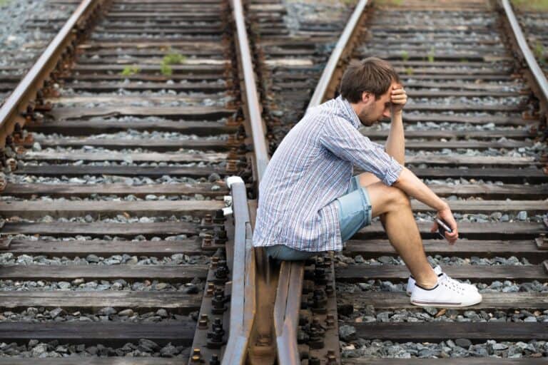 a man sitting on rail tracks going in different directions contemplating a change in life