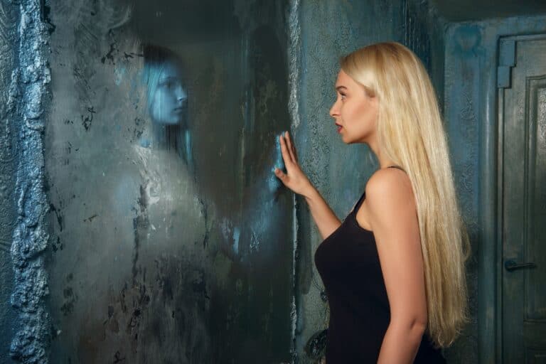 young woman looking to the mirror and seeing in reflection of someone else
